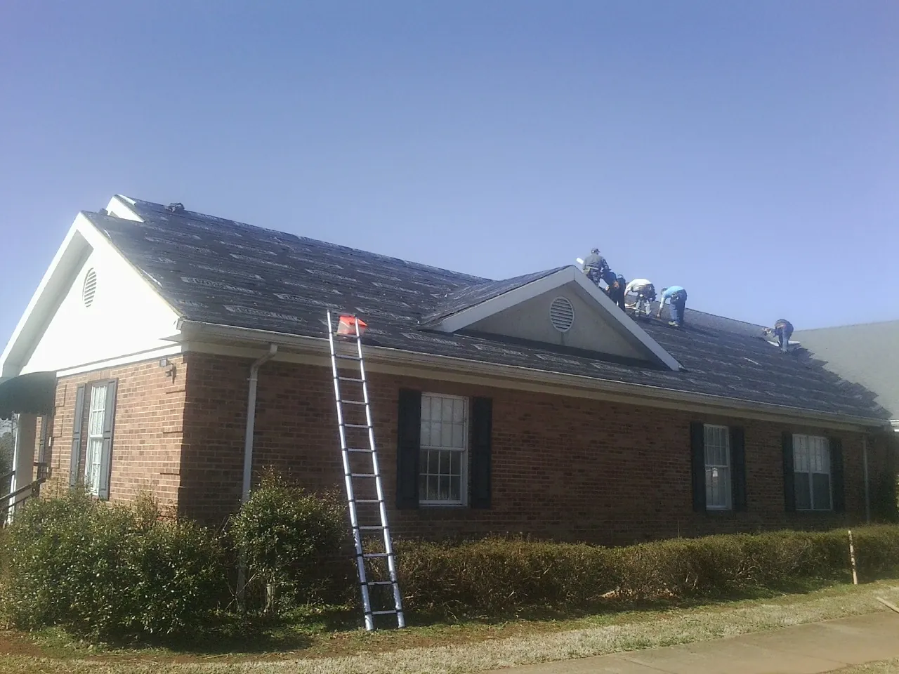 Crew tearing shingles off a brick ranch roof with a ladder set — Emergency Roof Repair work by our crew in Boonville