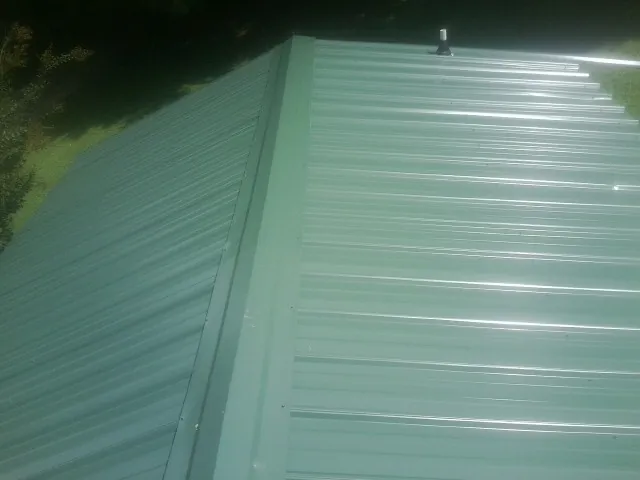New green metal panels meeting at the ridge of a roof — Flat Roof Repair work by our crew in Boonville