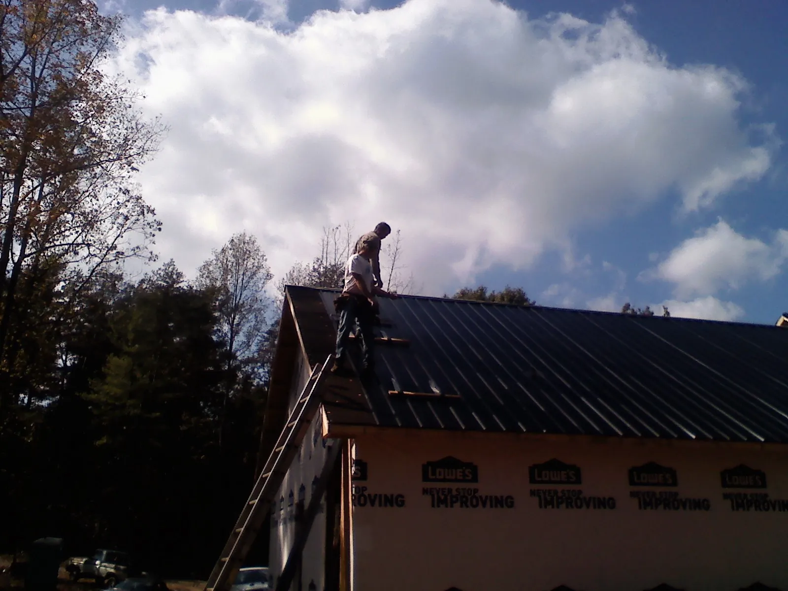 Roofer fastening dark metal panels high against a cloudy sky, from a Roof Inspection job in Boonville