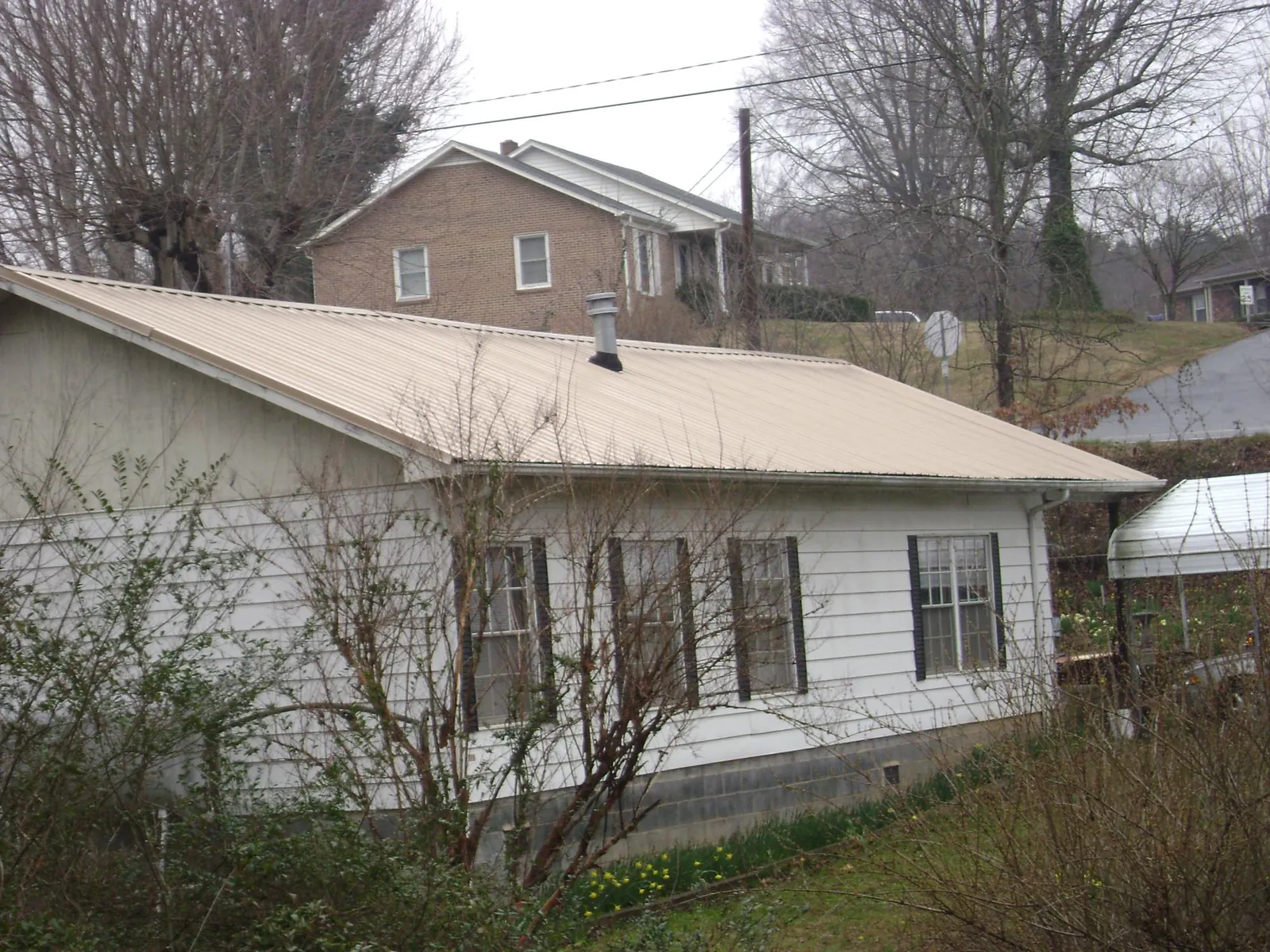 Tan metal roof on a white sided house set into a hillside — Commercial Roofing by Roofing Brothers in Boonville